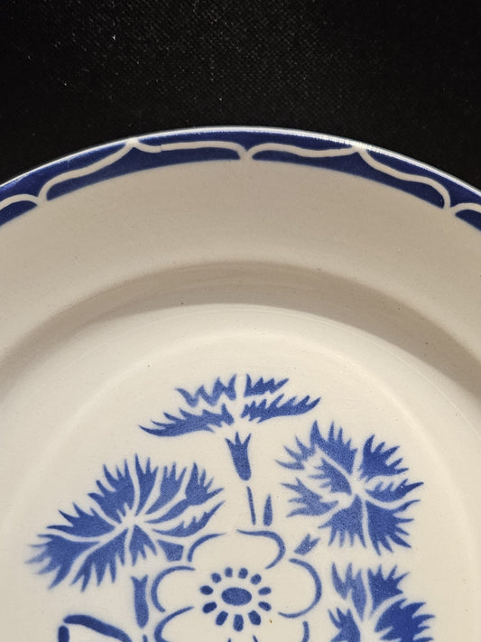 Détail de la bordure de l'assiette en demi-porcelaine Keller & Guerin Lunéville modèle Annecy, montrant le motif de vagues entrelacées réservées en blanc sur fond bleu cobalt, sur fond noir.