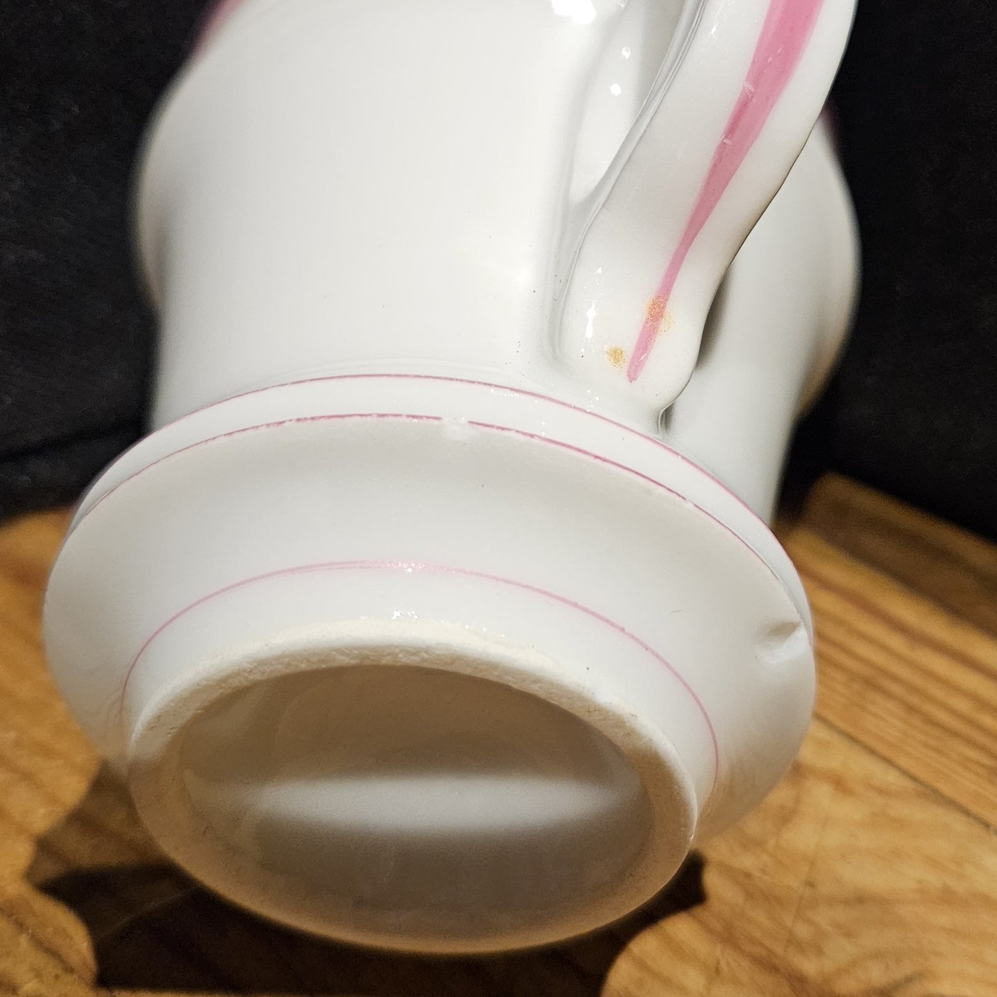 Vue du dessous de la tasse à brûlot en faïence blanche, montrant la base ovale avec des filets roses, et deux petits éclats visibles sur le pied de la tasse.