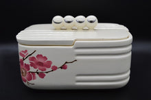 Charger l'image dans la galerie, Boite à biscuit en faïence de Saint-Amand. Cette boite de forme rectangulaire est typique Art Deco. Son couvercle est surmonté de 4 boules crème avec chacune un petit décor argenté en forme de virgule.  des fleurs de cerisier roses décorent cette boite , ce qui lui donne un coté japonais.