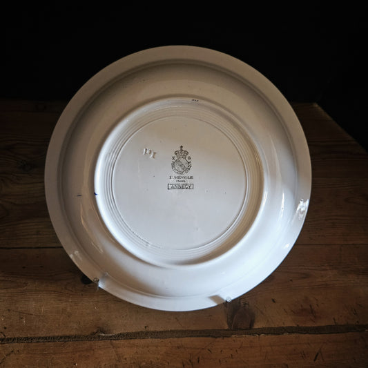 Vue du dos du plat creux en porcelaine opaque Keller & Guerin Lunéville modèle Annecy, montrant le fond blanc ivoire avec le poinçon manufacture et le numéro de moule 121 en relief dans la pâte, posé sur un présentoir en métal chromé sur fond bois.