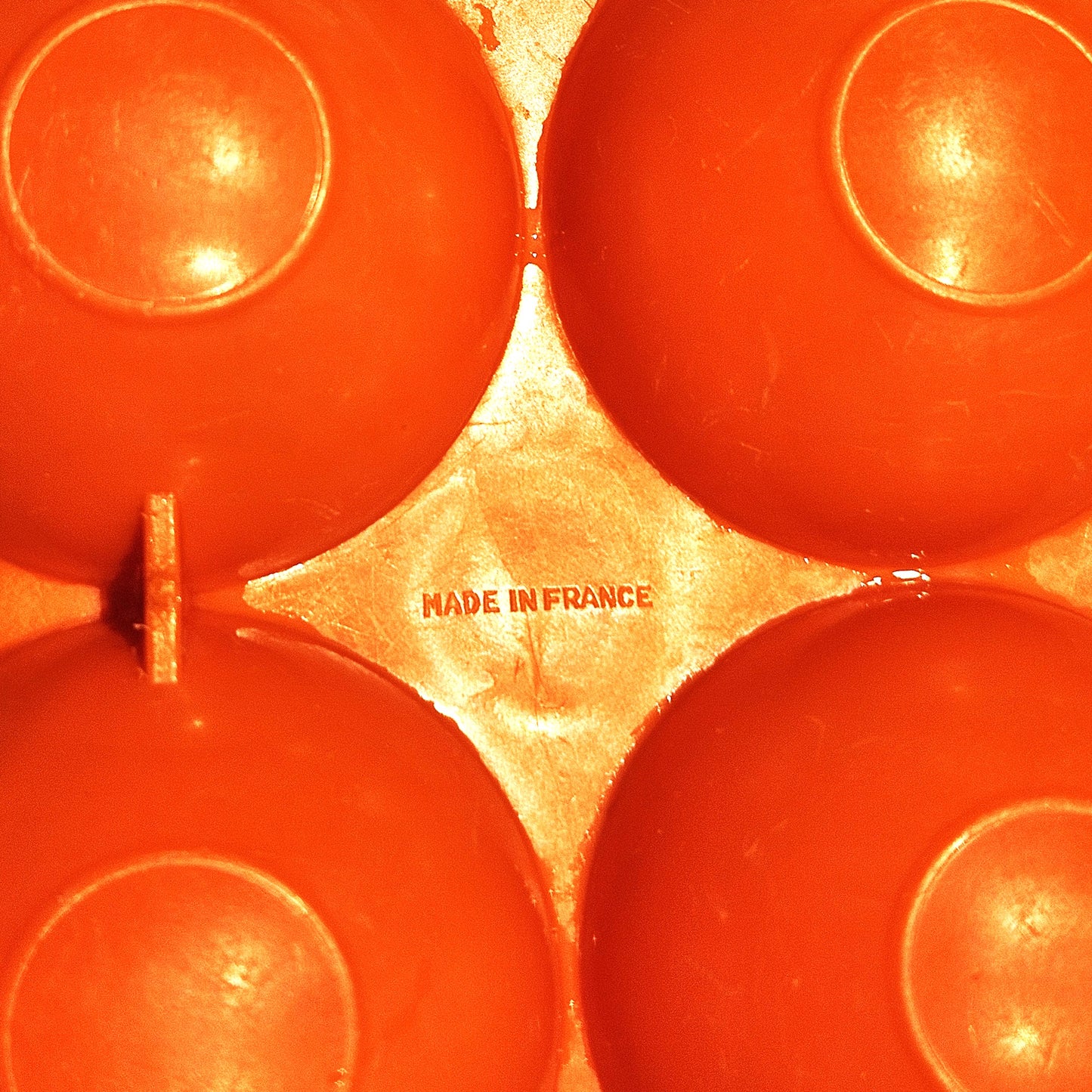 Gros plan sur le marquage Made in France moulé  dans le plastique orange vif de la boîte à œufs vintage, visible entre les alvéoles bombées, sur fond orange.