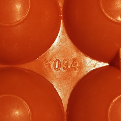 Gros plan sur le marquage 3094 moulé  dans le plastique orange vif de la boîte à œufs vintage, visible entre les alvéoles bombées, sur fond orange.