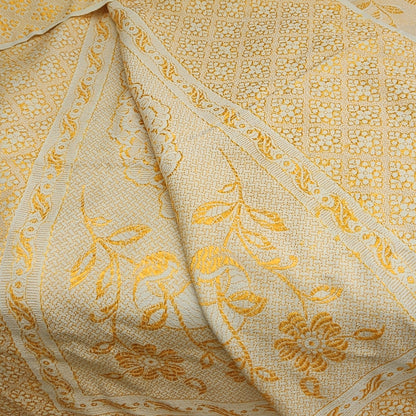 Détail de la frise florale à feuillages et rinceaux du jeté de canapé en jacquard double face années 1950-1960, montrant les deux faces du tissu en repli — fond crème/or chaud côté endroit et fond or/jaune intense côté envers — avec résille de petits motifs géométriques en nid d'abeilles visible sur le fond.