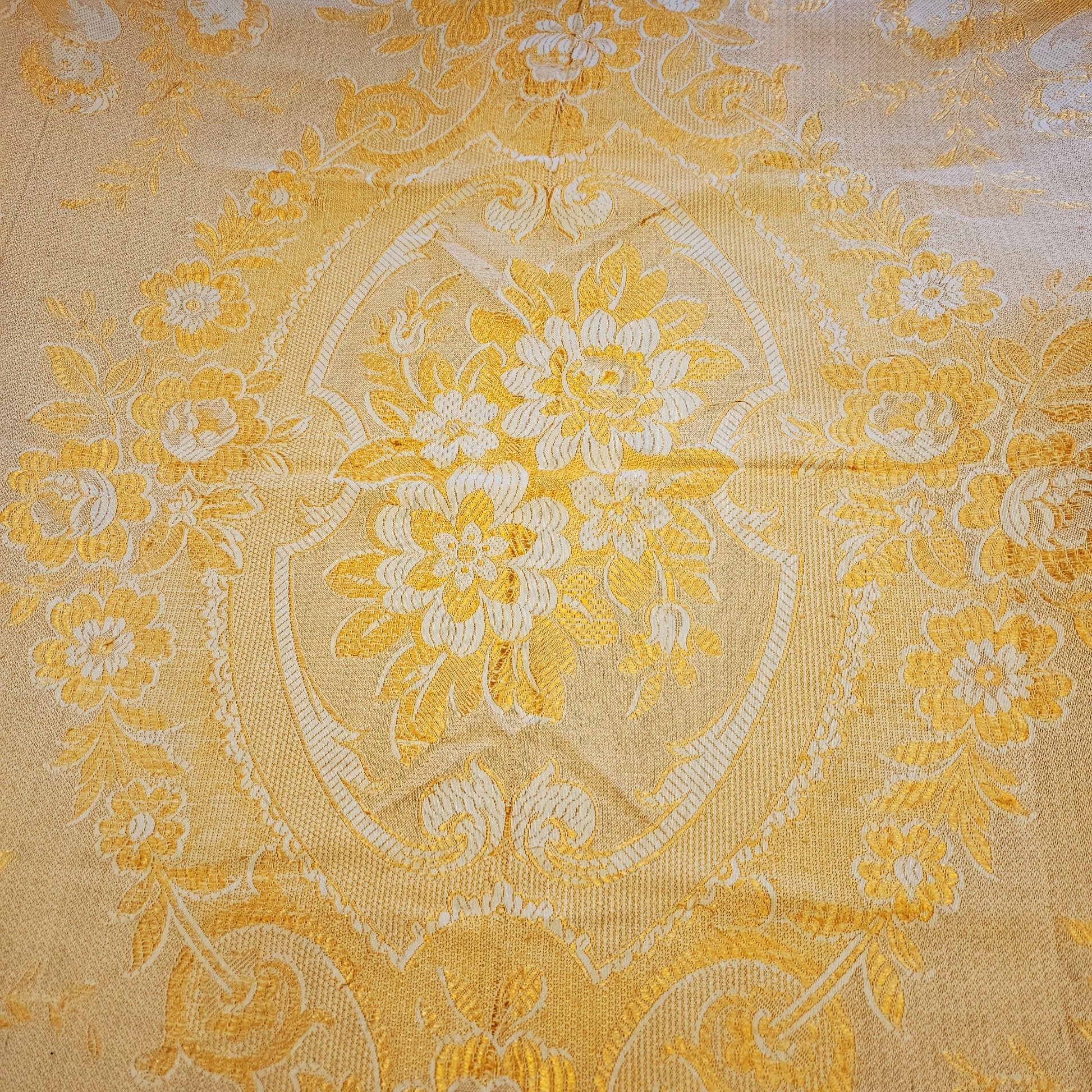 Détail du médaillon central en cartouche à écusson du jeté de canapé en jacquard double face années 1950-1960, face endroit fond crème/or, montrant le bouquet de pivoines et anémones finement tissées entouré de rinceaux et volutes Baroque, avec frise florale à roses en bordure.