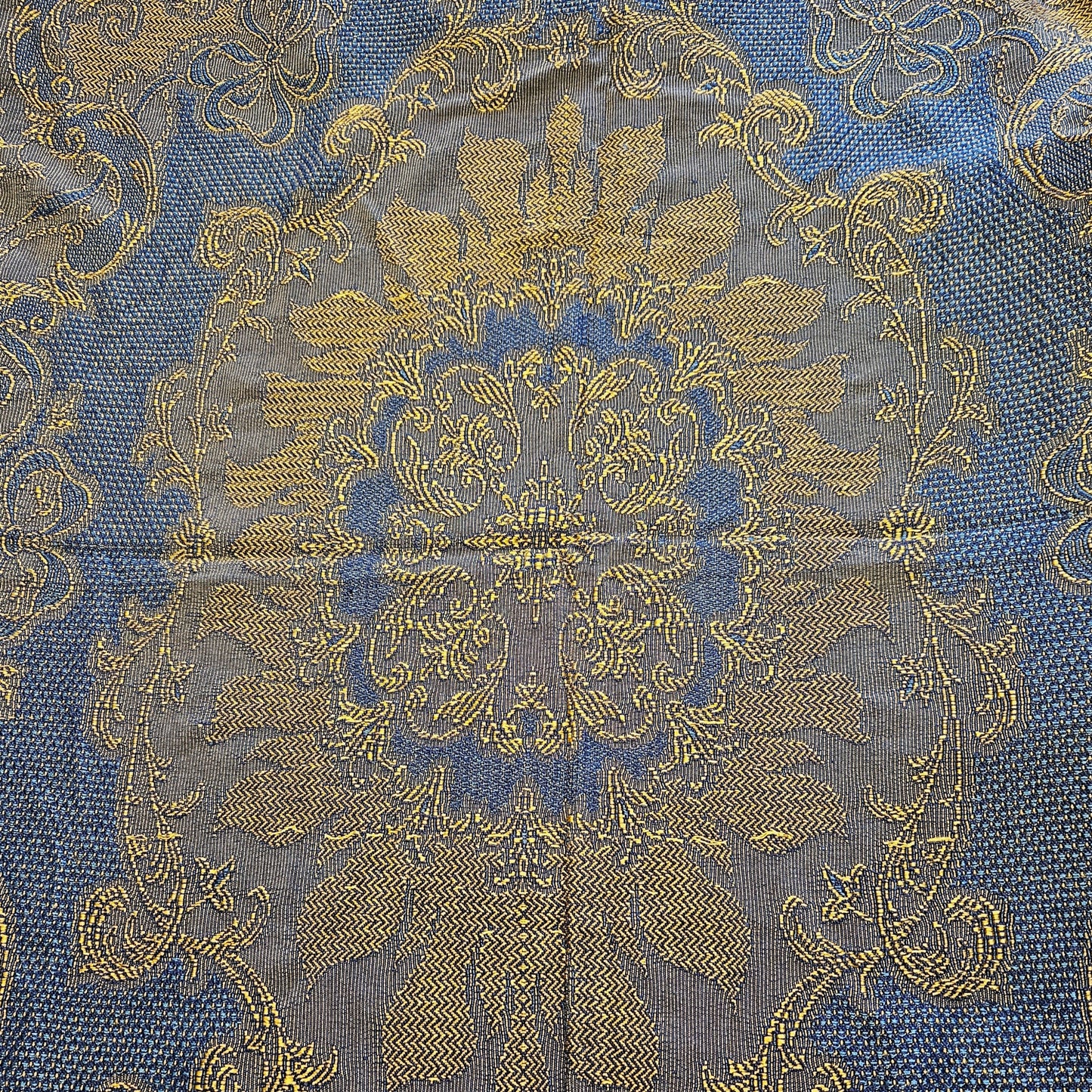Détail du médaillon central du jeté de canapé en jacquard double face années 1950-1960, face endroit bleu roi, montrant le vase fleuri symétrique avec bouquet de fleurs et feuillages en jaune doré, encadré de bandes à chevrons et rinceaux latéraux en volutes, sur fond bleu roi intense.