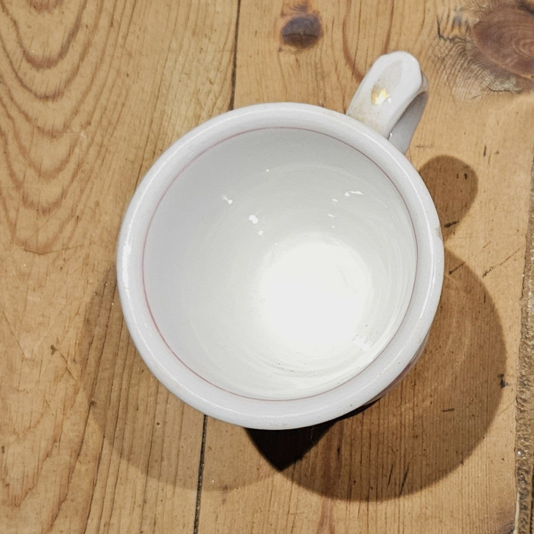 Vue plongeante de l'intérieur de la tasse à brûlot en faïence blanche, montrant l'émail blanc légèrement craquelé et l'anse ronde, posée sur une surface en bois brut.