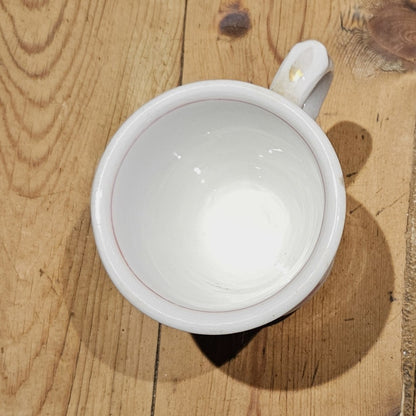 Vue plongeante de l'intérieur de la tasse à brûlot en faïence blanche, montrant l'émail blanc légèrement craquelé et l'anse ronde, posée sur une surface en bois brut.
