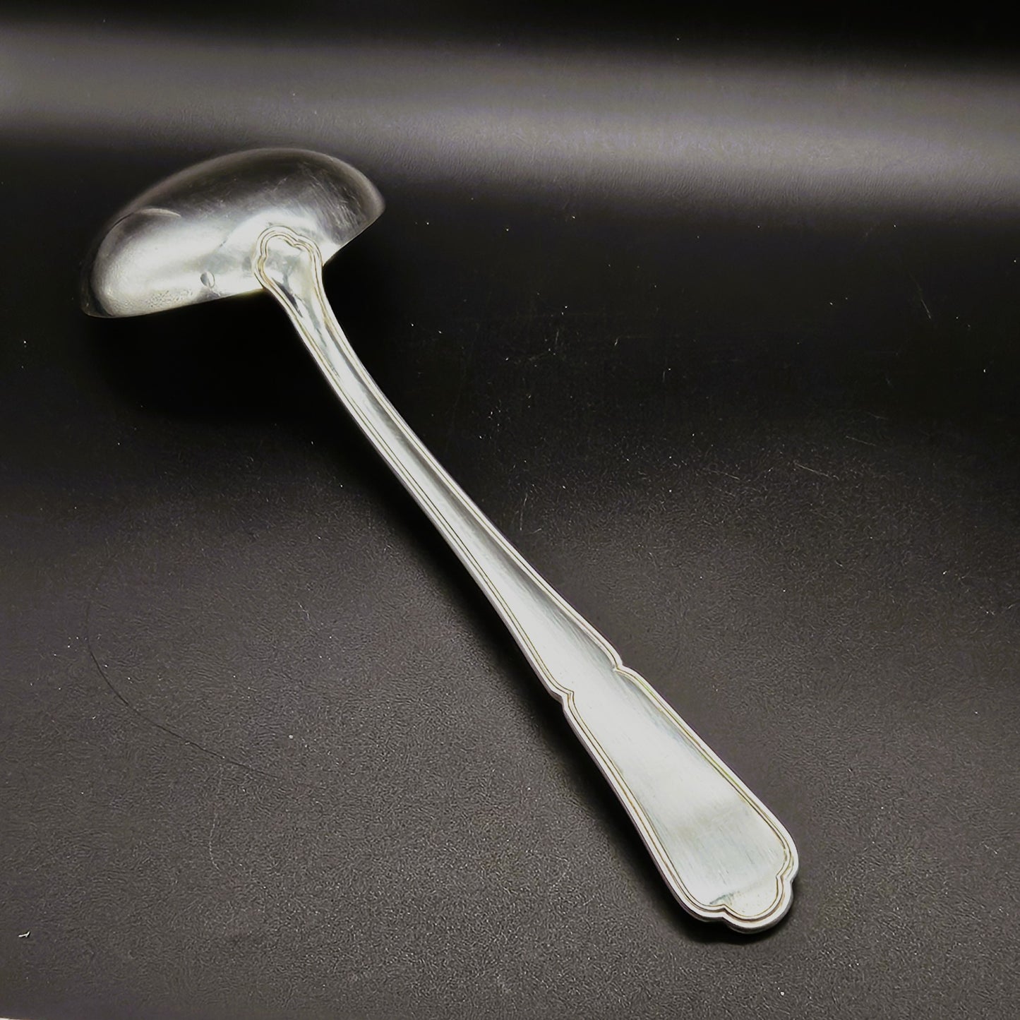 Louche à potage en métal argenté modèle Filet contour, 30,5 cm, vue de dos sur fond noir, montrant le dos de la cuillère ronde et le manche long légèrement incurvé à double filet.