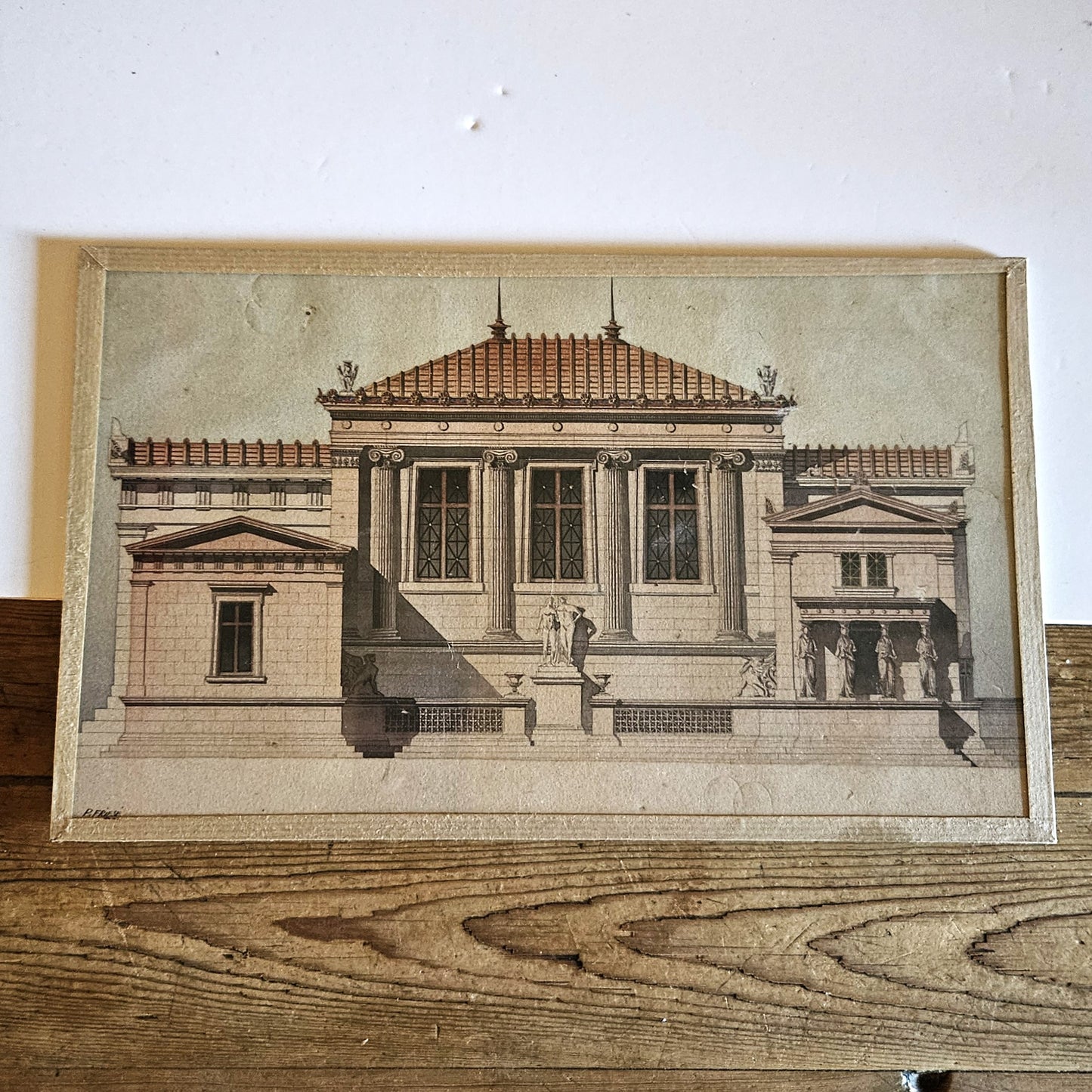 Aquarelle originale encadrée de Paul Friesé, représentant la façade d'un édifice public néo-classique colossal avec colonnes ioniques géantes, portique à cariatides, groupe sculpté monumental sur perron et toit à charpente apparente en caissons rouge brique, dans un cadre en papier texturé beige/doré, posée contre un mur blanc.