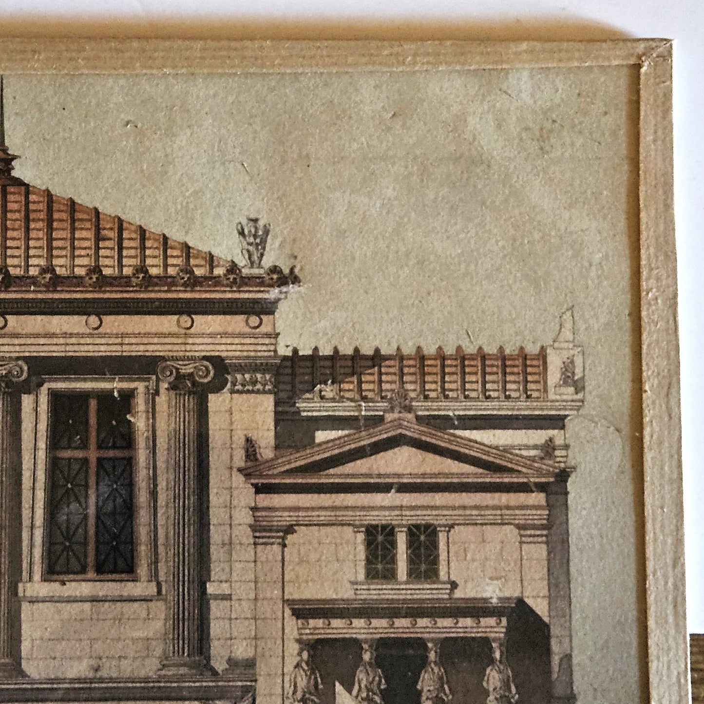 Détail du coin supérieur droit de l'aquarelle de Paul Friesé, montrant l'aile droite de l'édifice néo-classique avec toit à charpente apparente, acrotère en vase à flammes et colonnes ioniques, dans un cadre en papier texturé beige/doré.