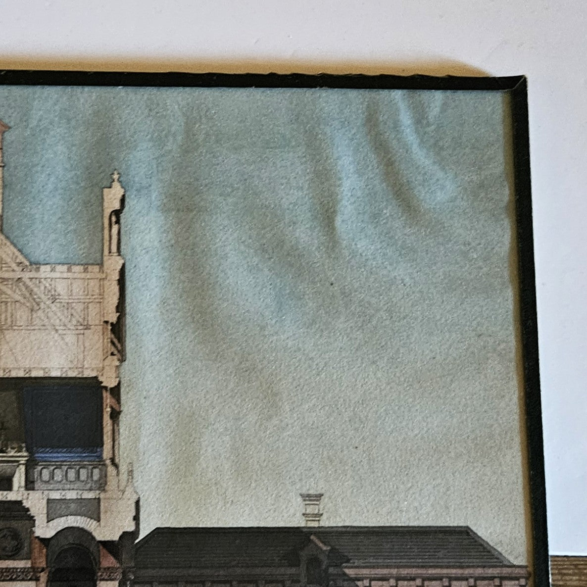 Détail de l'aquarelle de Paul Friesé, montrant la tour gothique centrale de l'édifice monumental éclectique avec pinacles,  et croix de faîtage en ardoise bleue, et le gondolage important du papier dans le coin supérieur droit du au collage de l'œuvre sur le carton de fond, dans un cadre en papier texturé noir.