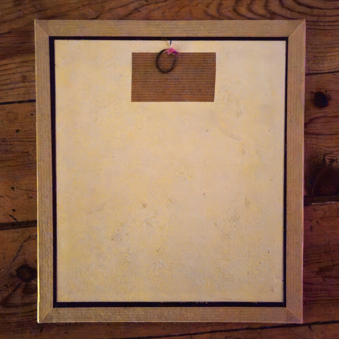 Vue du dos du cadre du plan d'architecture de Paul Friesé, montrant un fond en carton beige avec un anneau de suspension central fixé par une étiquette en kraft, dans un cadre sous-verre entouré de kraft.