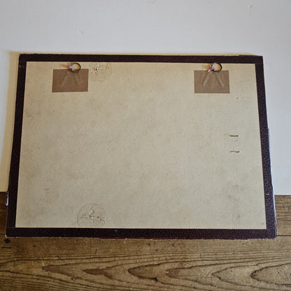 Vue du dos du cadre de l'aquarelle de Paul Friesé, montrant un fond en carton beige avec deux anneaux de suspension fixés par des étiquettes en kraft  dans un cadre en papier texturé brun foncé, posé sur un parquet en bois brut.