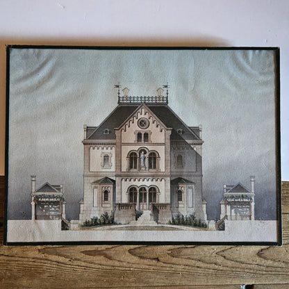 Vue d'ensemble de l'aquarelle originale encadrée attribuée à Paul Friesé, représentant la façade d'un édifice religieux néo-roman avec statue de la Vierge à l'Enfant, perron monumental et pavillons latéraux, dans un sous verre entouré d'un papier noir d'origine, posée sur une table en bois brut.