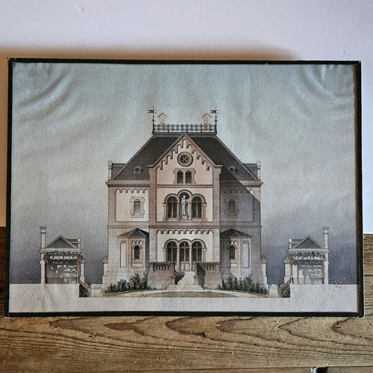 Vue d'ensemble de l'aquarelle originale encadrée attribuée à Paul Friesé, représentant la façade d'un édifice religieux néo-roman avec statue de la Vierge à l'Enfant, perron monumental et pavillons latéraux, dans un sous verre entouré d'un papier noir d'origine, posée sur une table en bois brut.