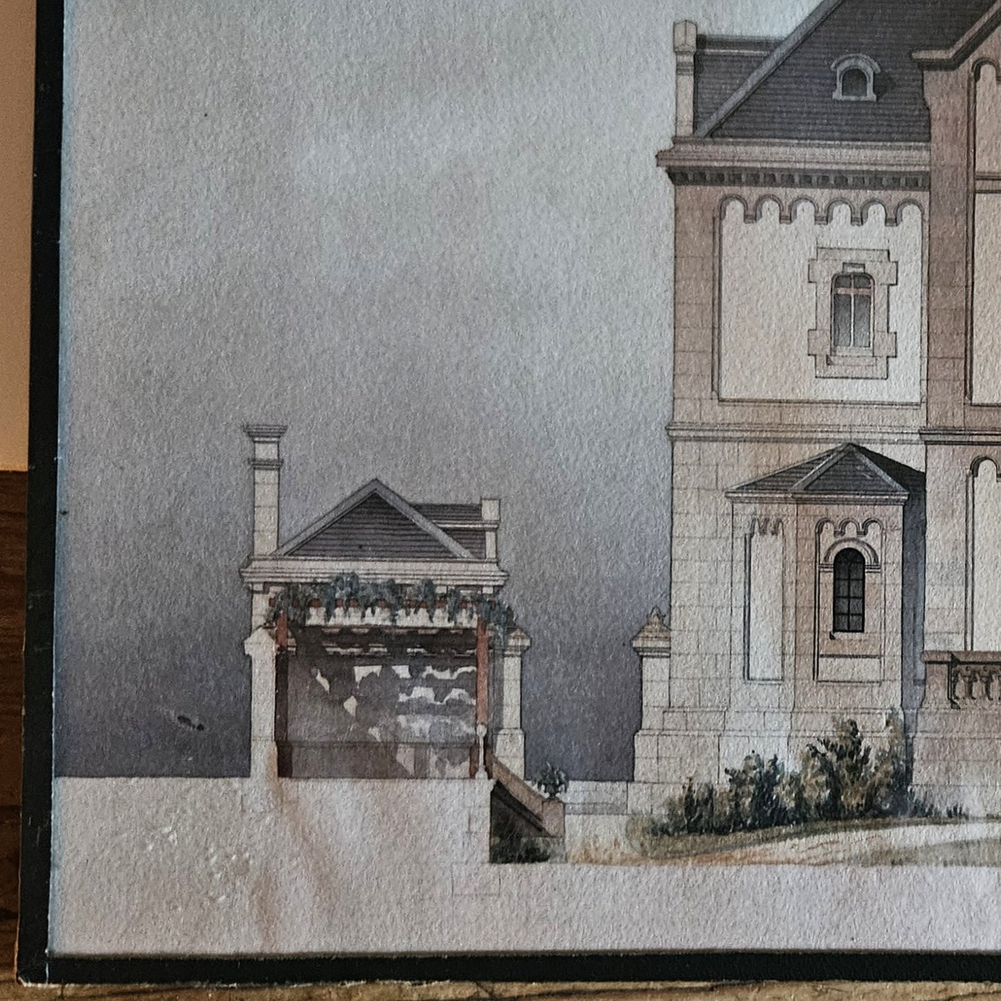 Détail de l'aquarelle attribuée à Paul Friesé, montrant l'aile droite de l'édifice religieux néo-roman avec pavillon latéral à toiture en pavillon, posé sur une table en bois brut.