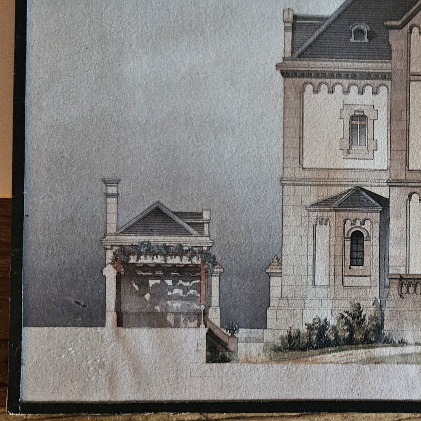 Détail de l'aquarelle attribuée à Paul Friesé, montrant l'aile droite de l'édifice religieux néo-roman avec pavillon latéral à toiture en pavillon, posé sur une table en bois brut.