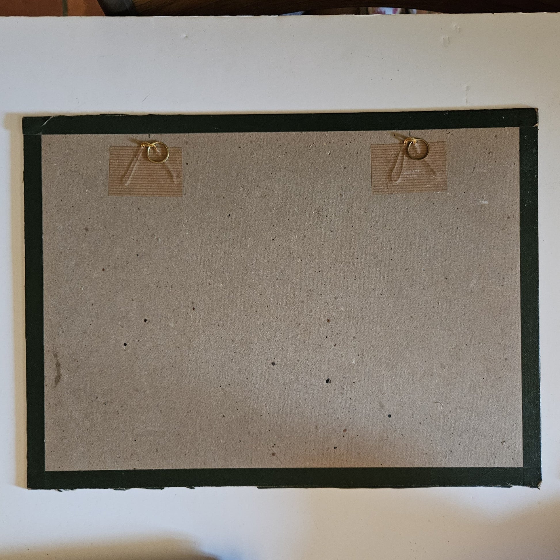 Vue du dos du cadre de l'aquarelle attribuée à Paul Friesé, montrant un fond en carton gris avec deux anneaux de suspension dorés fixés par des étiquettes en kraft,  posé sur un fond blanc