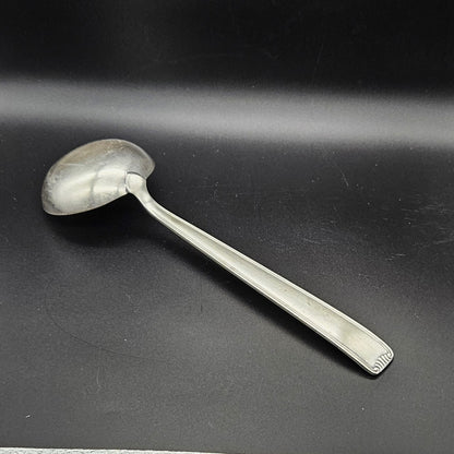 Louche à potage en métal argenté Art Déco, 31 cm, vue de dos sur fond noir, montrant le dos de la cuillère ronde et le manche rectangulaire à double filet latéral avec extrémité en éventail à cannelures.