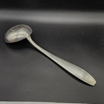 Louche à potage en métal argenté Art Déco, 32,5 cm, vue de dos sur fond noir, montrant le dos de la cuillère ronde et le manche fusiforme effilé à filet central unique avec extrémité à carrés géométriques en relief.