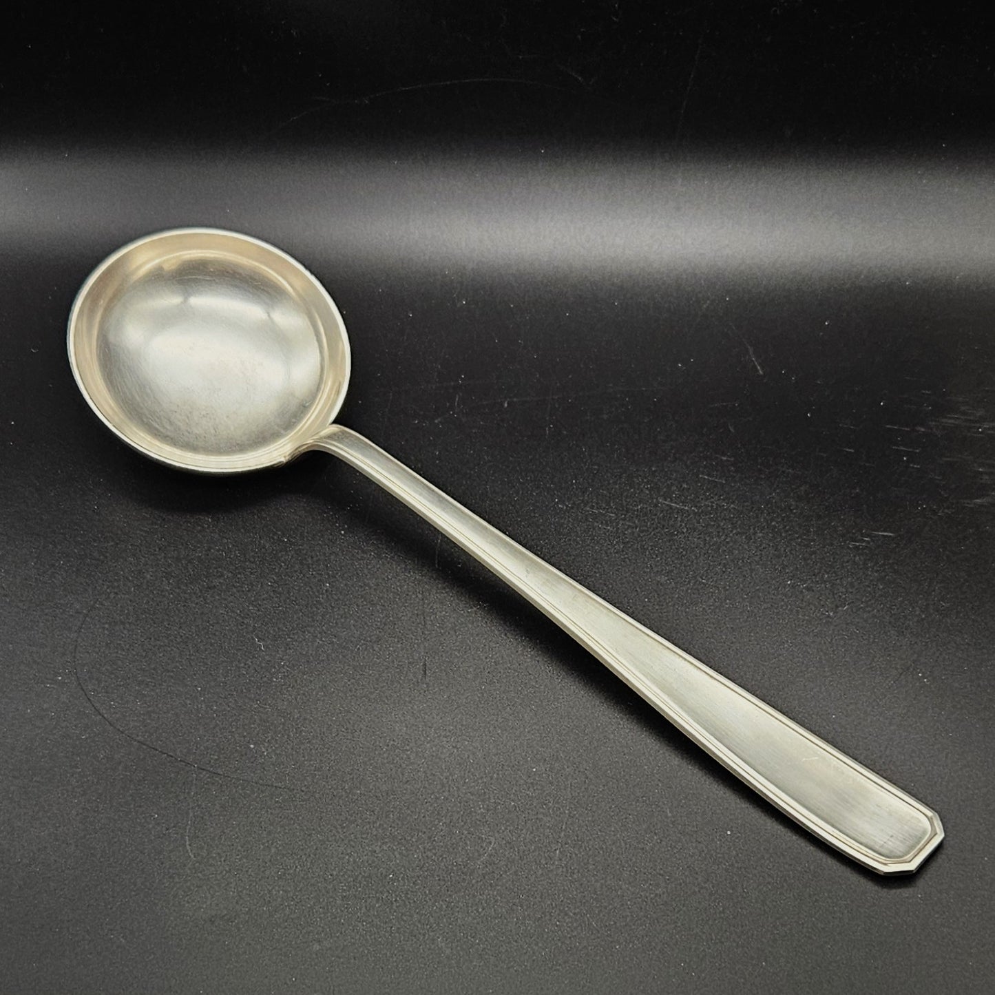Louche à potage en métal argenté modèle de la Maison Boulenger Paris, 33,7 cm, vue de face sur fond noir, montrant la cuillère ronde et profonde avec bourrelet périphérique et le manche rectangulaire à filet périphérique unique avec extrémité à pans coupés octogonaux.