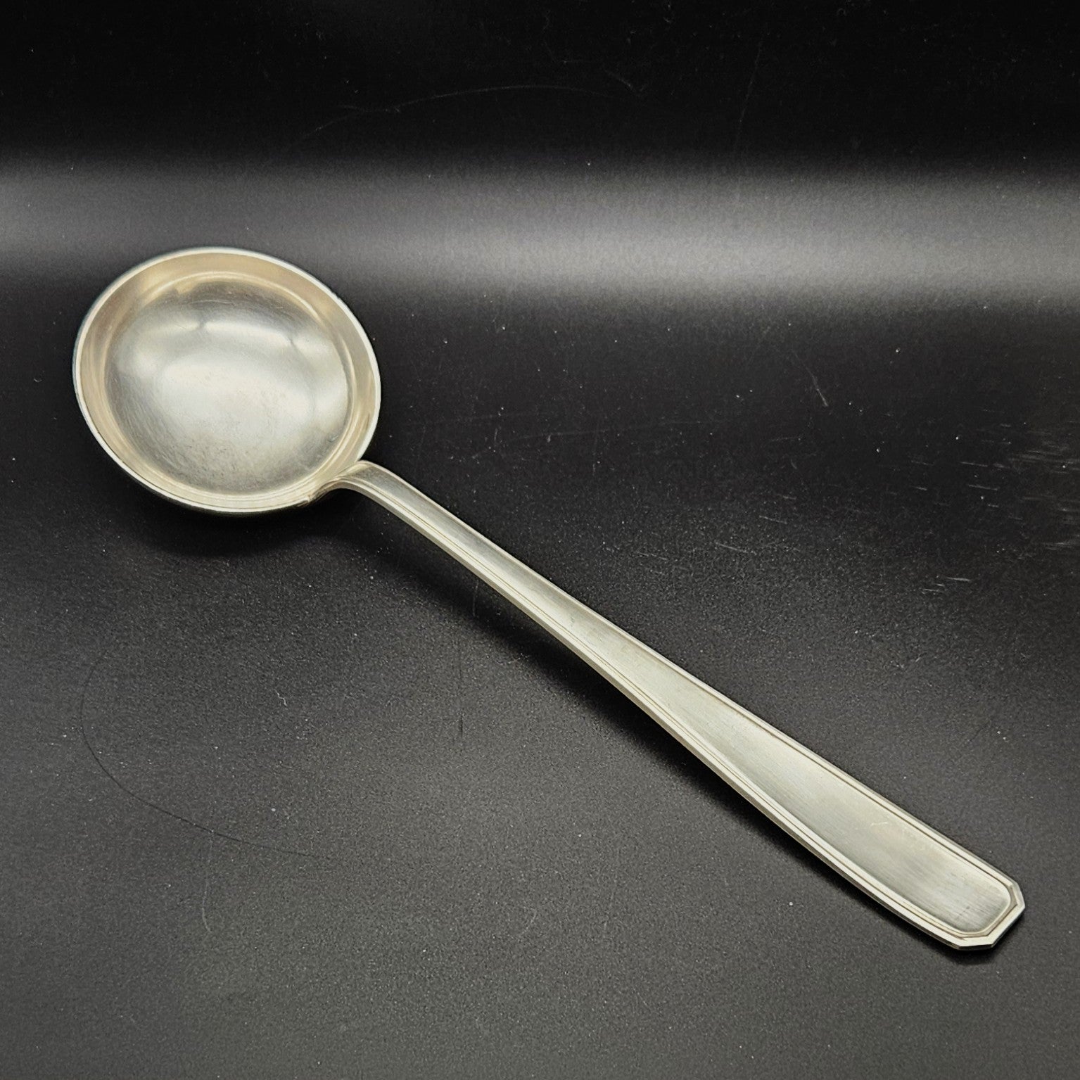 Louche à potage en métal argenté modèle de la Maison Boulenger Paris, 33,7 cm, vue de face sur fond noir, montrant la cuillère ronde et profonde avec bourrelet périphérique et le manche rectangulaire à filet périphérique unique avec extrémité à pans coupés octogonaux.