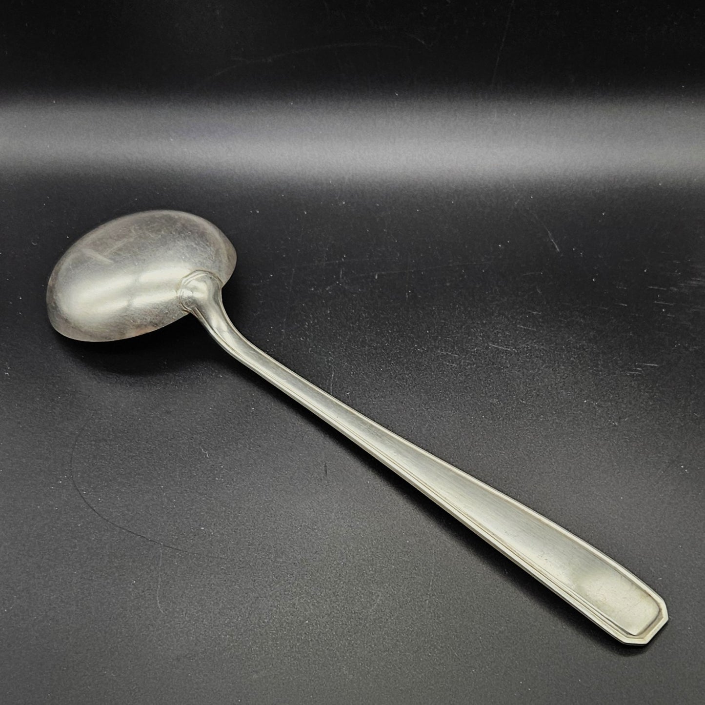 Louche à potage en métal argenté modèle de la Maison Boulenger Paris, 33,7 cm, vue de dos sur fond noir, montrant le dos de la cuillère ronde et le manche rectangulaire à filet périphérique unique avec extrémité à pans coupés octogonaux.