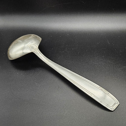 Louche à potage en métal argenté Art Déco, 31 cm, vue de dos sur fond noir, montrant le dos de la cuillère ronde et le manche rectangulaire à double filet latéral convergent avec encoches en V aux angles.