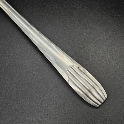 Gros plan sur l'extrémité arrondie du manche de la louche à potage en métal argenté Art Déco tardif, montrant les cinq cannelures en éventail et les trois cannelures longitudinales parallèles du manche, sur fond noir.