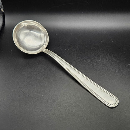 Louche à potage en métal argenté Art Déco, 31,7 cm, vue de face sur fond noir, montrant la cuillère ronde et profonde avec bourrelet périphérique et le manche à double filet latéral parallèle avec extrémité arrondie à motif en arc de cercle à quatre segments.