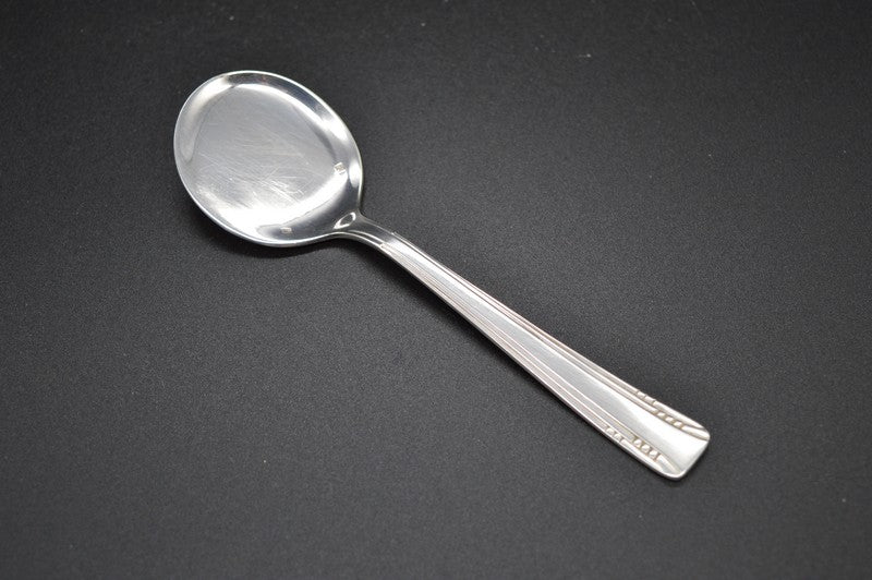 Une cuillère à glace posée à l'endroit pour voir le modèle Art Deco, très épuré et géométrique . Le manche  comporte 4 ciselures  qui partent de l'extrémité pour s'évanouir et ne faire plus qu'une au cuilleron. 3 petites ciselures horizontales entre le bord et la première ciselure, puis, plus bas, quatre ciselures horizontales entre les deux ciselures. ,